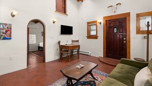 Un salón con una mesa de madera, un sofá verde, un televisor montado en la pared y una puerta de madera decorada con una cabeza de toro.