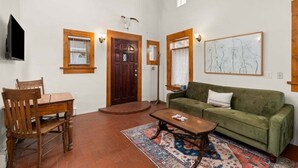 Una sala de estar con una mesa de madera, dos sillas, un sofá verde, un tapete estampado y techo de madera.