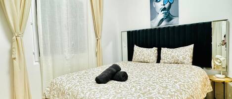 Een slaapkamer met een bed, gordijnen, een hoofdeinde, een nachtkastje en een aan de muur bevestigd kunstwerk.