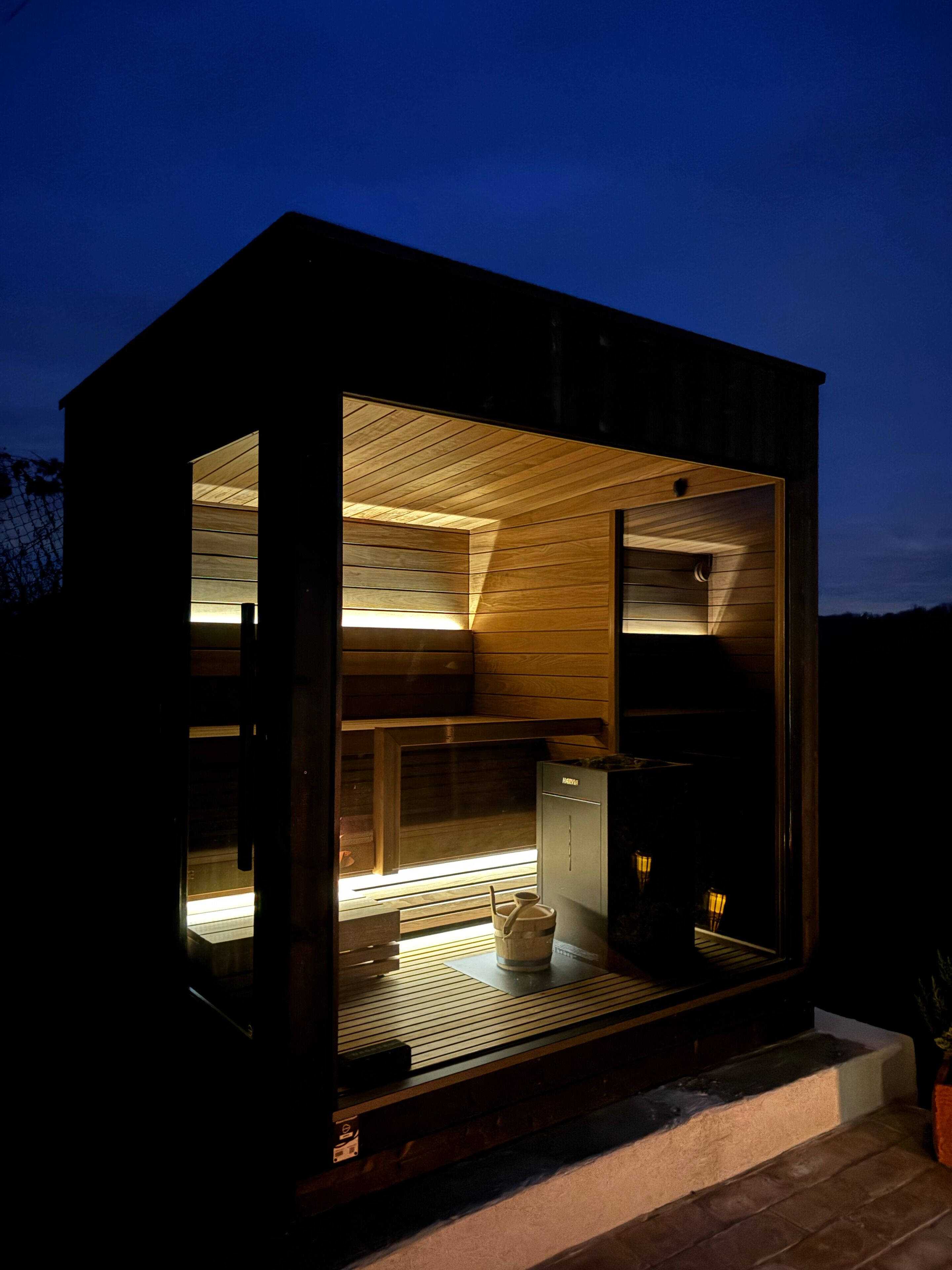 Una cabaña moderna y compacta con interior de madera y una pequeña cocina visible a través de una puerta abierta.