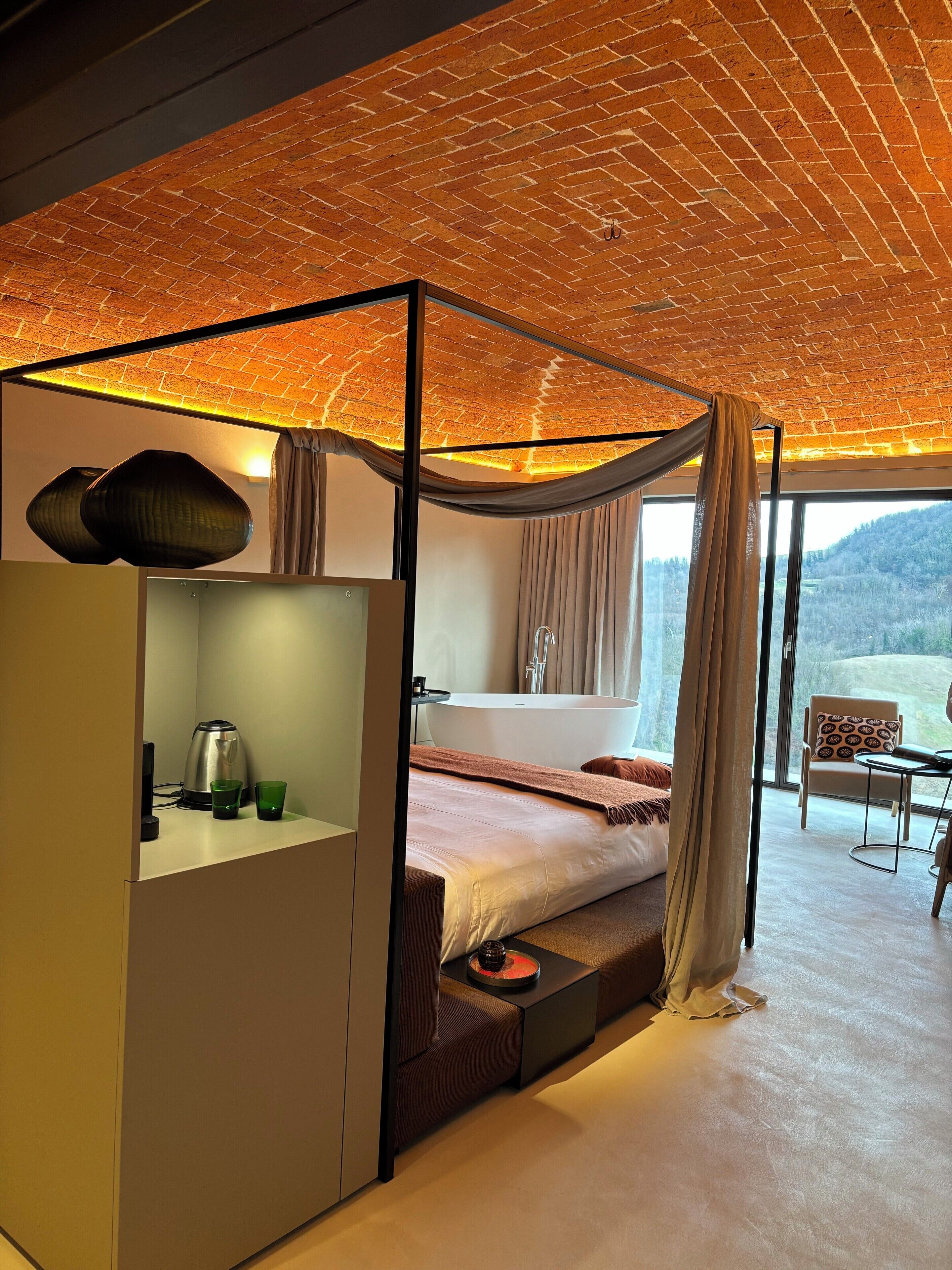 Ein modernes Schlafzimmer mit Baldachinbett, einer Sitzecke mit Blick und einem großen Fenster.