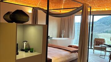 Ein modernes Schlafzimmer mit Baldachinbett, einer Sitzecke mit Blick und einem großen Fenster.