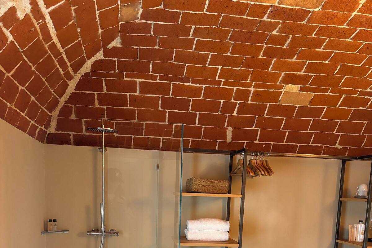 A modern bathroom with a glass shower enclosure, a built-in shelf with towels, and a brick ceiling.