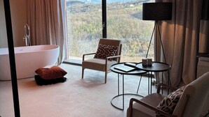 A modern room with a large window, a bathtub, two chairs, a small table, and a floor lamp. - Relais Dal Cavaliere (Moncalvo)