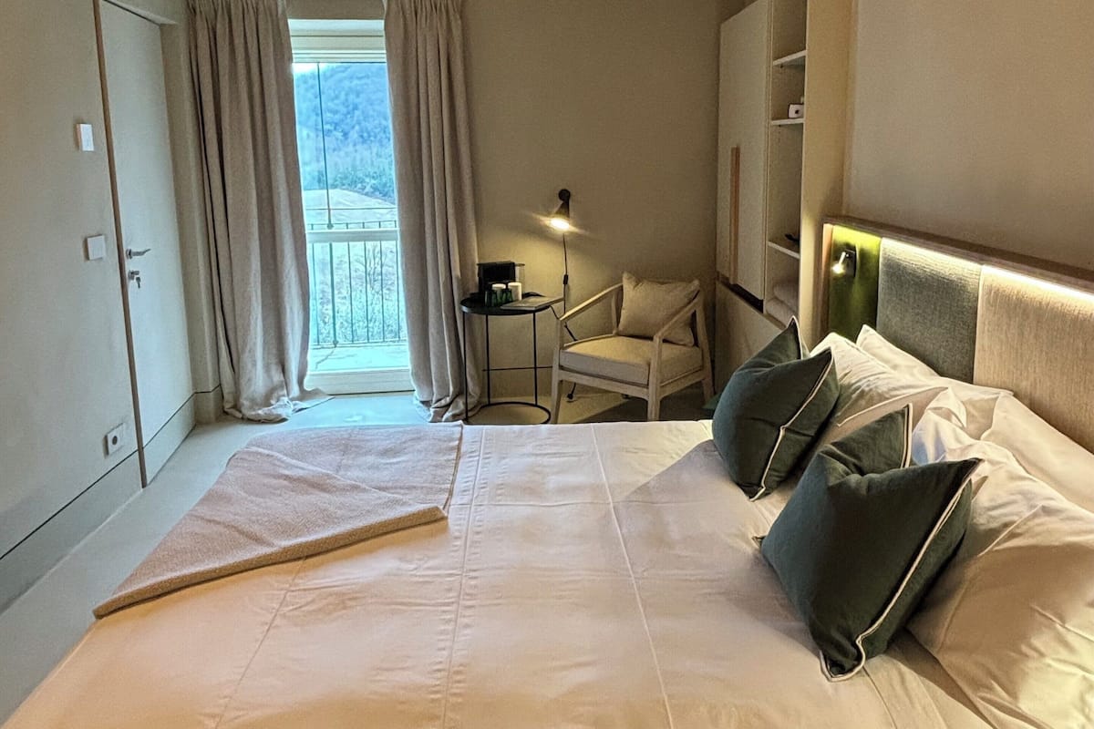 A hotel room with a bed, a chair, a lamp, and a view of the outdoors.