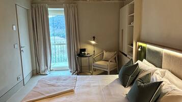 Quarto de hotel com cama, uma cadeira, uma luminária e vista para o exterior.