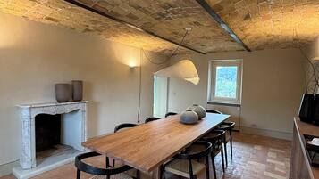 A dining area with a long wooden table, black chairs, a fireplace, and a brick ceiling.