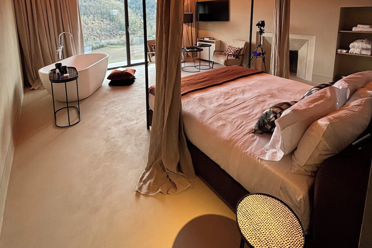 A bedroom with a brick ceiling, a large bed, a bathtub, and a view of the outdoors.