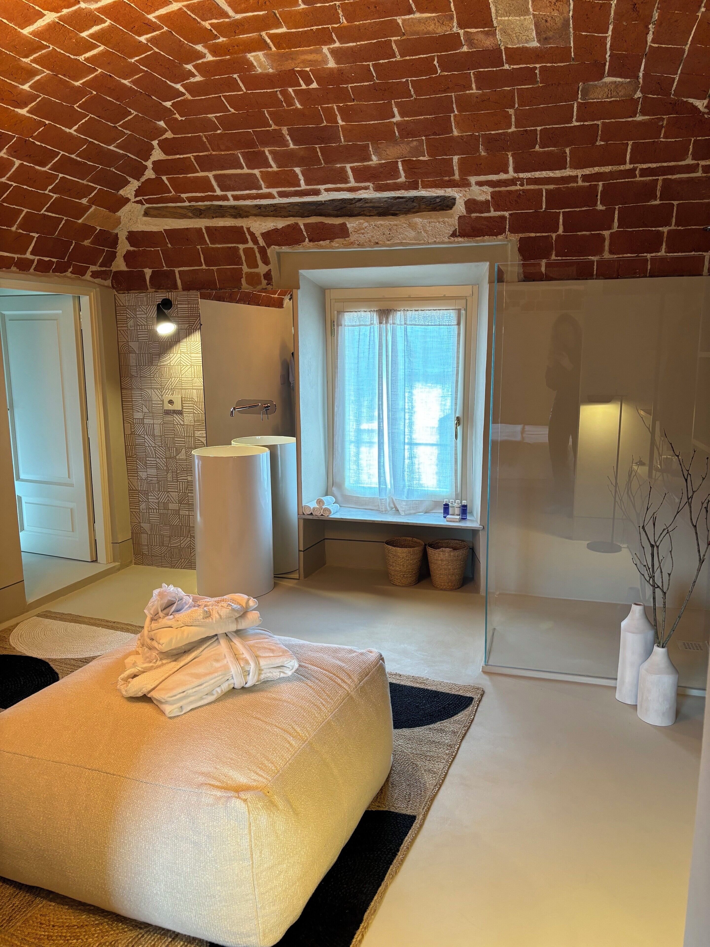 A modern bathroom with a brick ceiling, a large window with curtains, a bathtub, and a towel stack.
