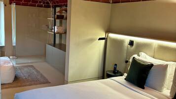 Una camera d'albergo moderna con soffitto in mattoni, un letto grande con lenzuola bianche, un comodino con una lampada e un altro piccolo comodino con un telefono.