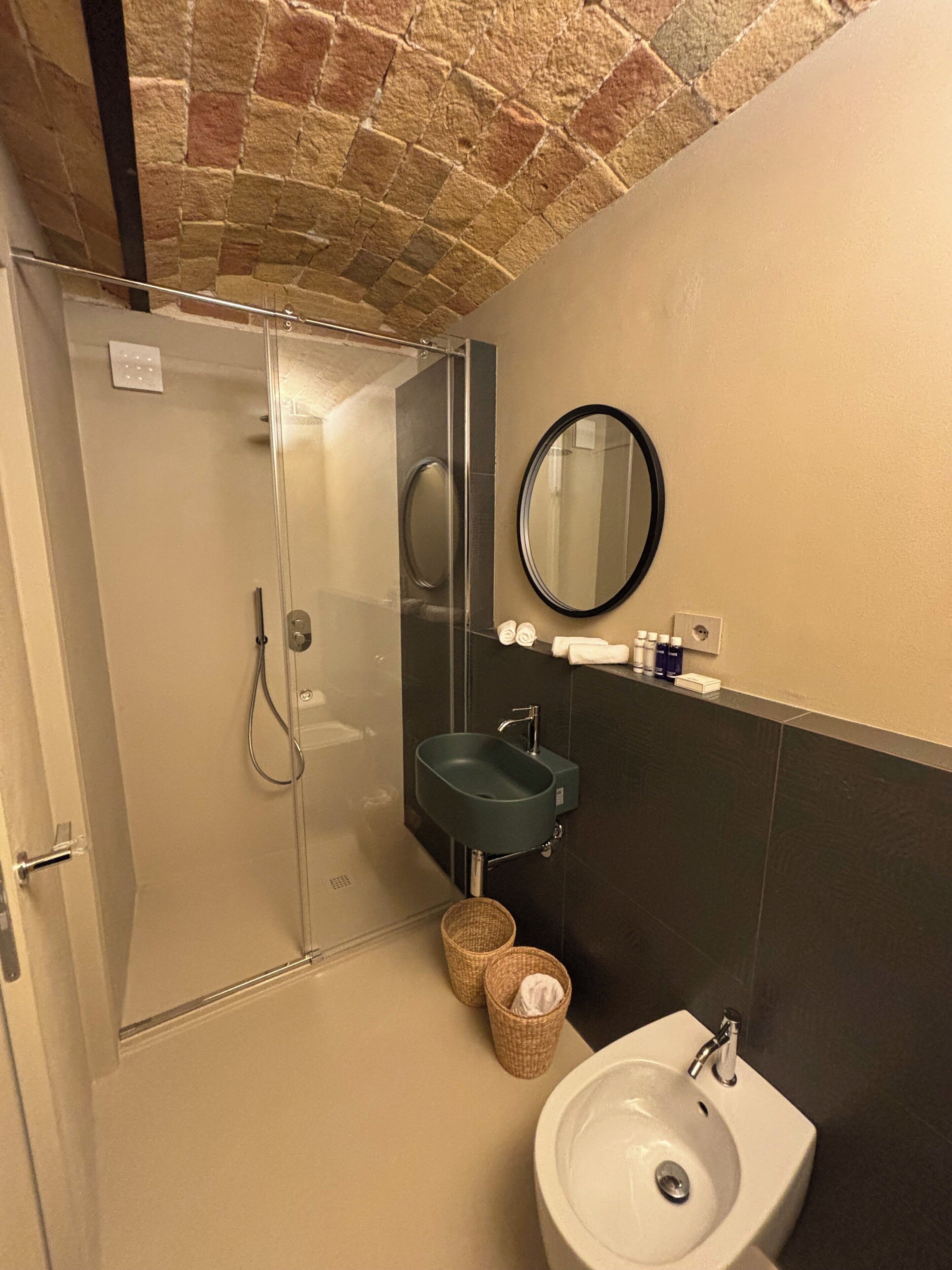 Un baño con ducha de vidrio, un lavabo, un espejo y pared con azulejos.