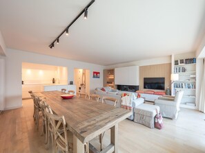 A modern living space with a wooden dining table, a sofa set, a TV, and a bookshelf. - Sunny Stay Near Brugge (Knokke-Heist)