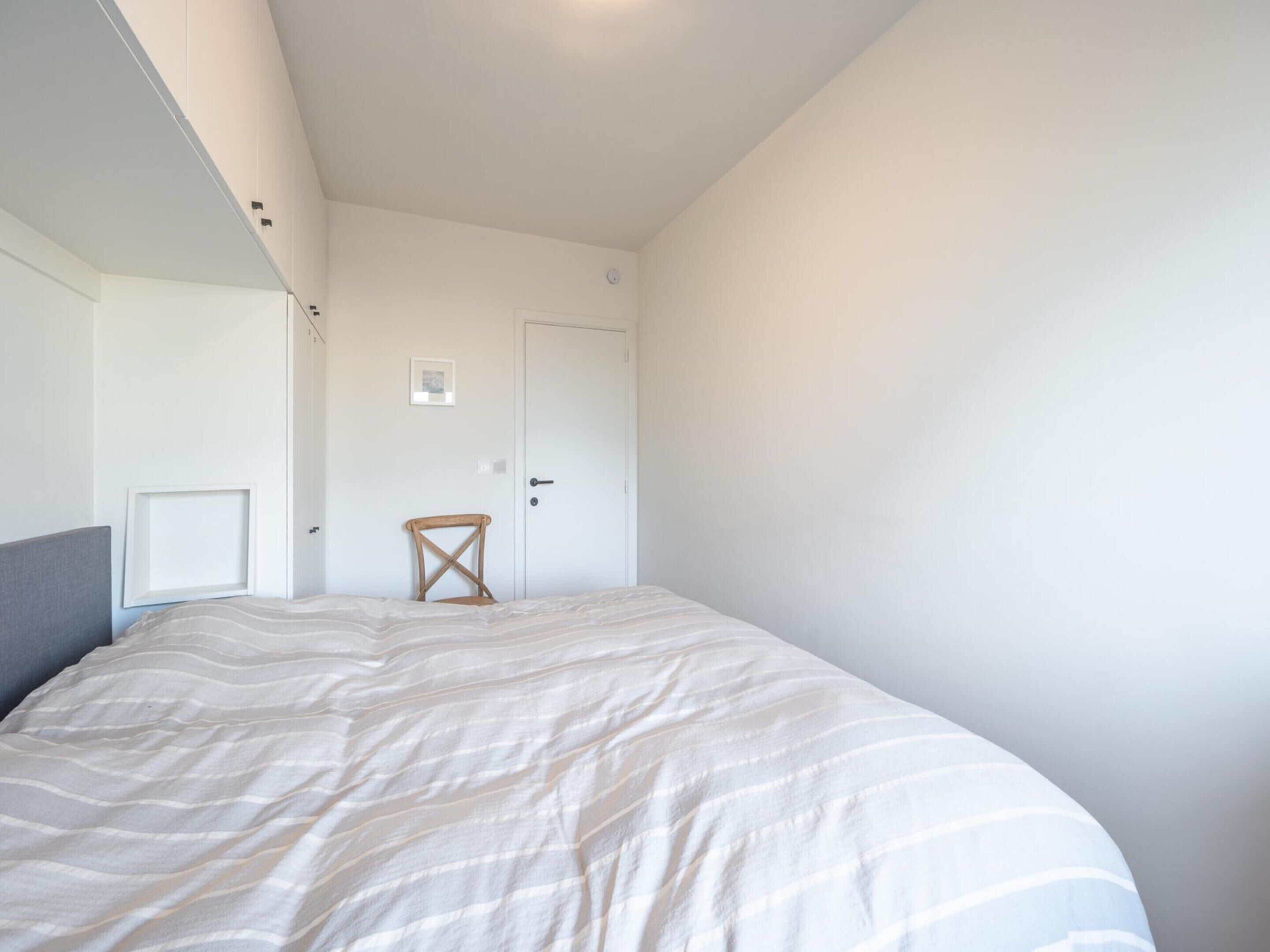 Una camera da letto con un letto, una sedia, una porta e un quadro appeso al muro.