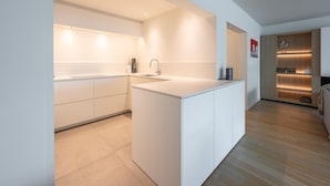 Une cuisine moderne avec des meubles blancs, un îlot central et un coin salon intégré avec un revêtement en bois.