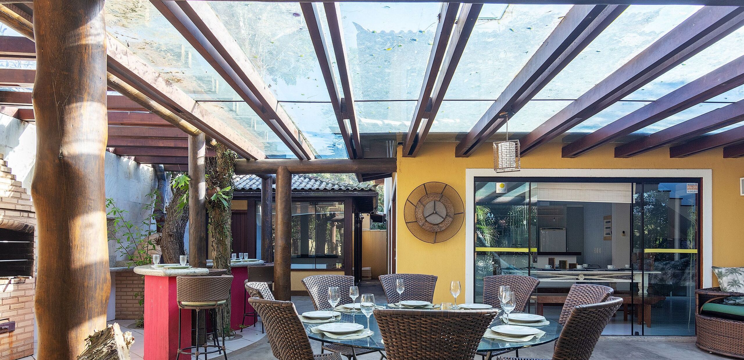 Un patio al aire libre con mobiliario de mimbre, una mesa de vidrio y un reloj en la pared.