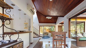 A modern kitchen with a dining area, featuring a wooden ceiling, large windows, and a wicker sofa. - Bz55 Casa 200m da praia com 4 suítes (Buzios)