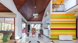 A spacious living area with a wooden ceiling, a colorful wall, and a view of the outdoors. - Bz55 Casa 200m da praia com 4 suítes (Buzios)