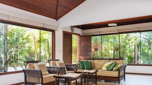 A room with large windows, wicker furniture, and a view of lush greenery. - Bz55 Casa 200m da praia com 4 suítes (Buzios)
