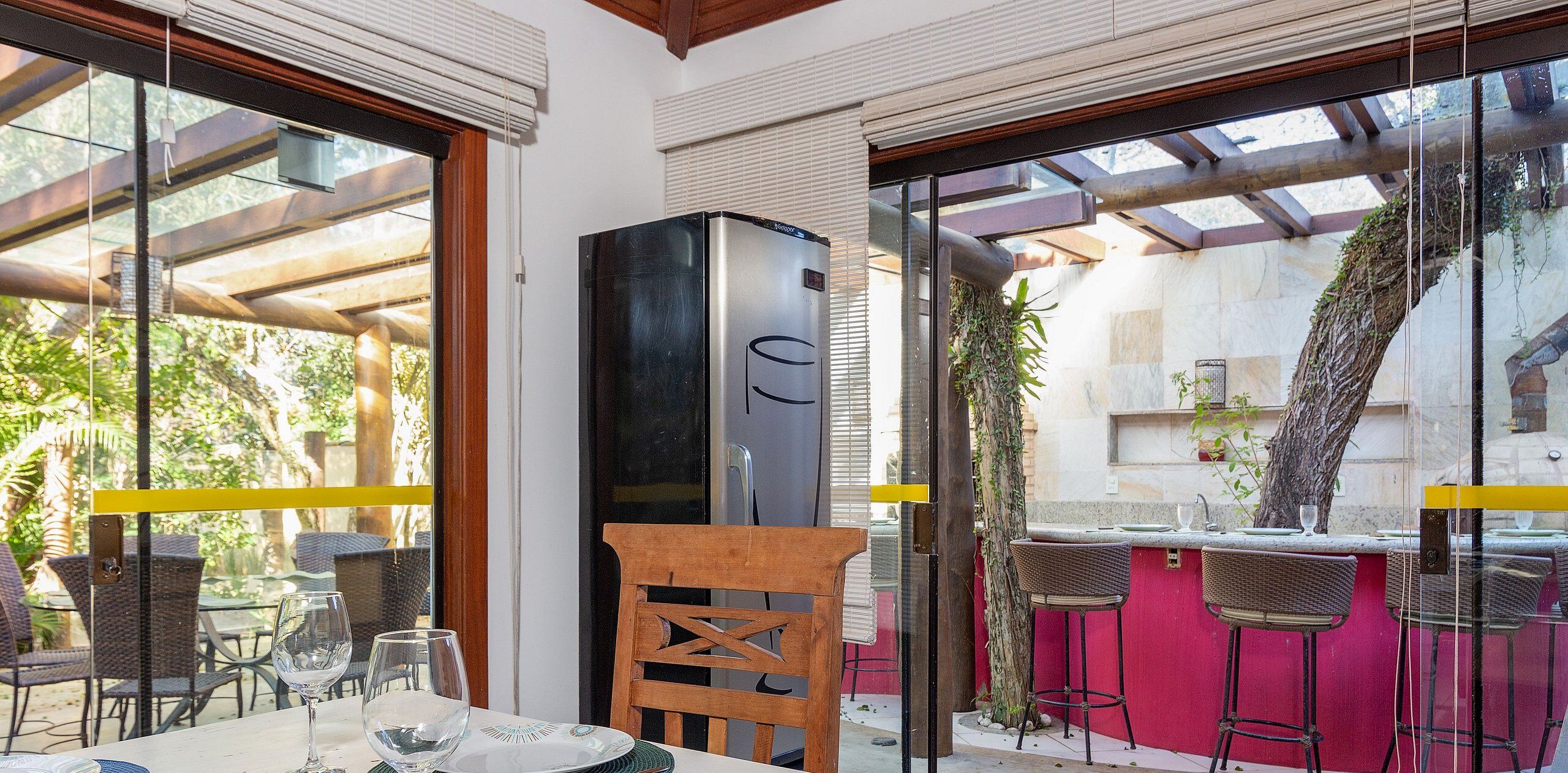 Un espace extérieur aménagé pour les repas, avec des chaises et des tables en osier, un réfrigérateur noir et un comptoir de bar rouge.