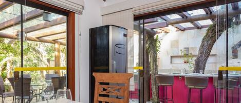 Un espace extérieur aménagé pour les repas, avec des chaises et des tables en osier, un réfrigérateur noir et un comptoir de bar rouge.