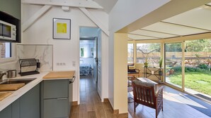 A modern kitchen with a built-in microwave, a sink, and a wooden countertop. There is a dining area with a table and chairs, and a view of a garden through large windows. - Gîte between the Seine and the cliffs near GIVERNY and the Château de la Roche Guyon (Gommecourt)