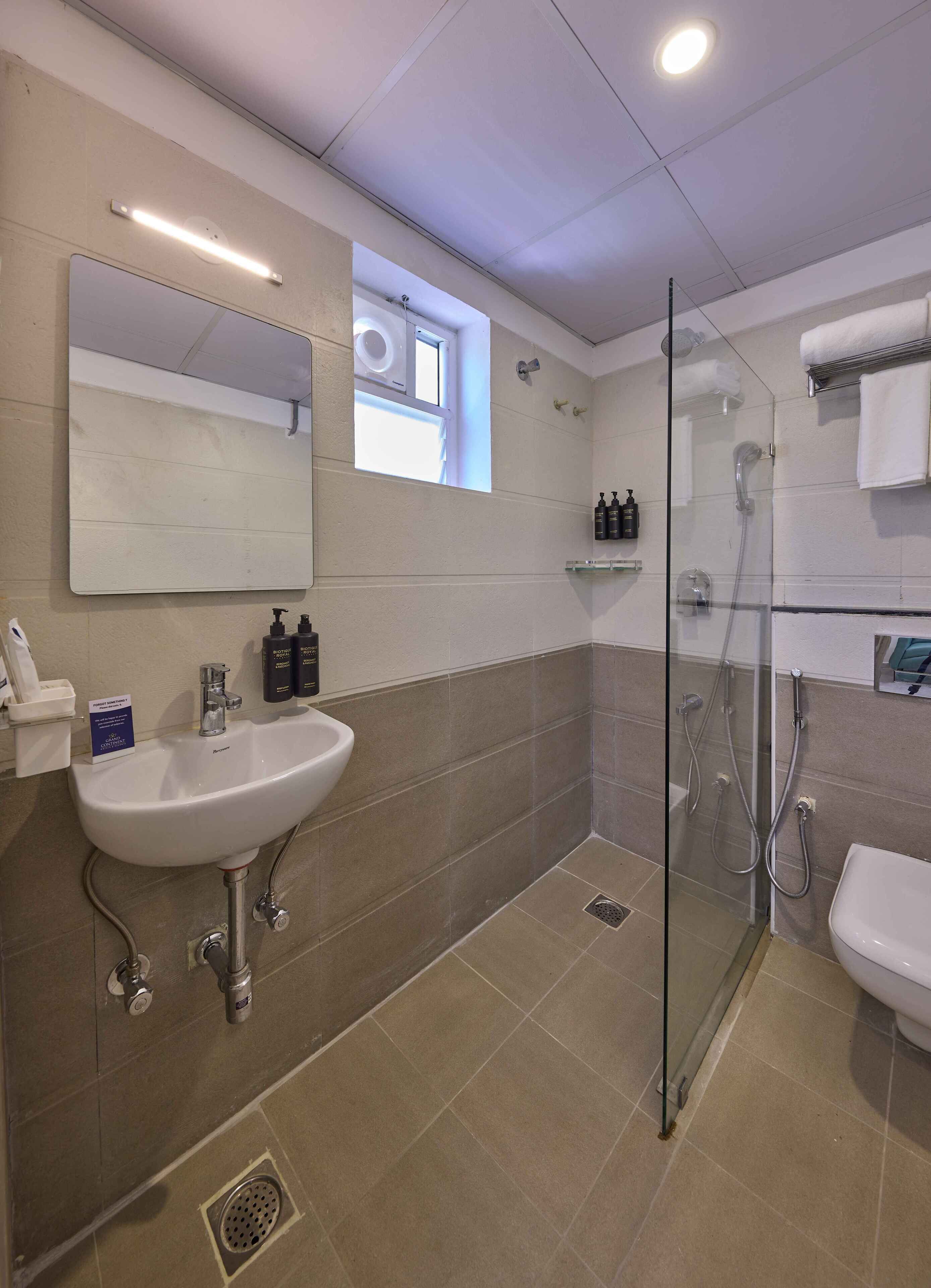 Un baño moderno con un espejo grande, un lavabo, una ducha con mampara de vidrio y un inodoro.