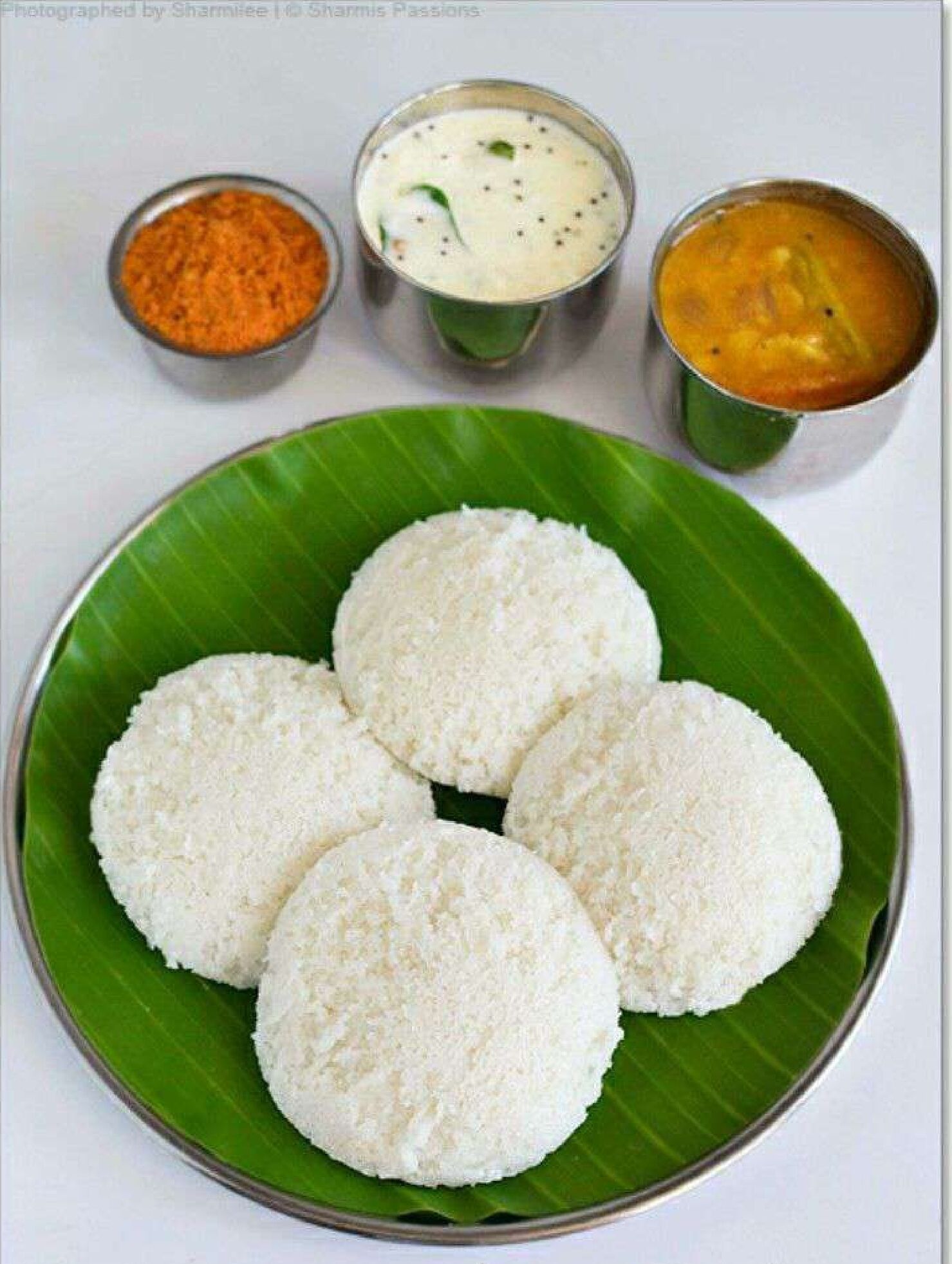A plate of white rice balls on a green leaf, accompanied by three small bowls of different sauces.