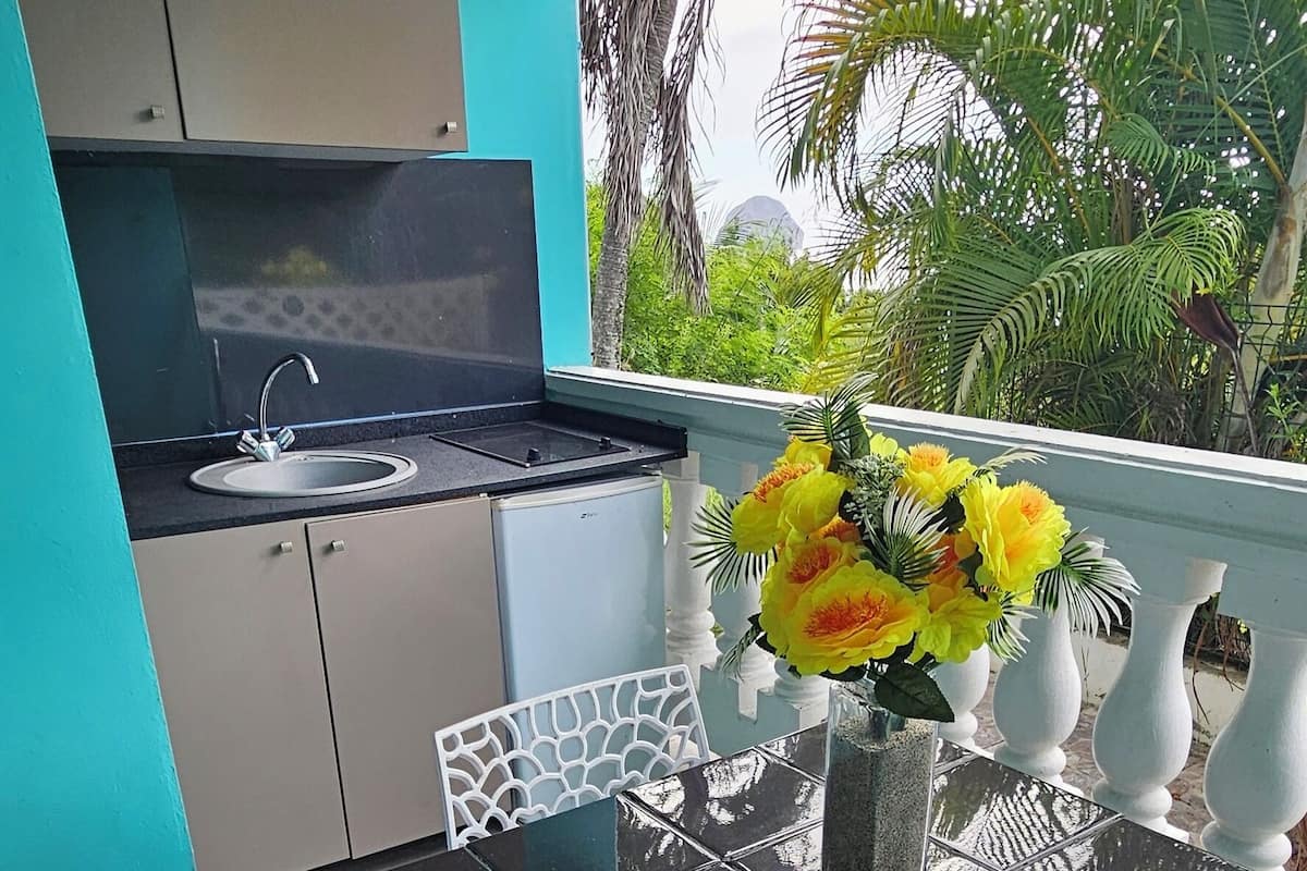 A kitchen with a sink and cabinets, a dining table with a vase of flowers, and a view of palm trees.