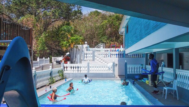 Un espace piscine avec vue sur un bâtiment, une personne debout près de la piscine et une chaise sur la terrasse.