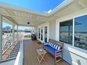 A covered outdoor deck with a wooden bench, a small table, and a lounge chair.