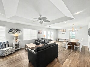 A spacious living area with a ceiling fan, a dining table with chairs, and a sofa with patterned cushions.