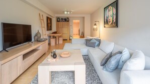 A modern living room with a flat-screen TV, a wooden coffee table, a sofa with patterned cushions, and a painting on the wall. - Apartment in Knokke-heist Near Lippenslaan (Knokke-Heist)