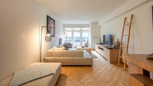 A modern living room with a sofa, a TV, and a wooden table. - Apartment in Knokke-heist Near Lippenslaan (Knokke-Heist)