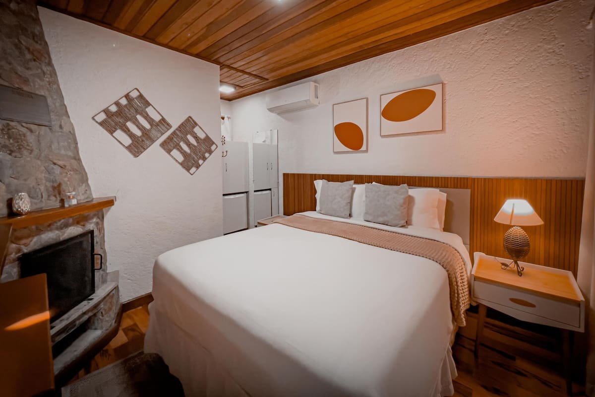 A bedroom with a bed, a nightstand, a lamp, a fireplace, and two refrigerators.
