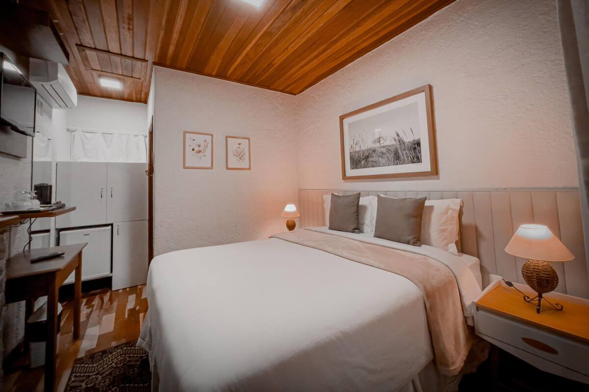 A bedroom with a bed, bedside table, lamp, and a wall-mounted picture.