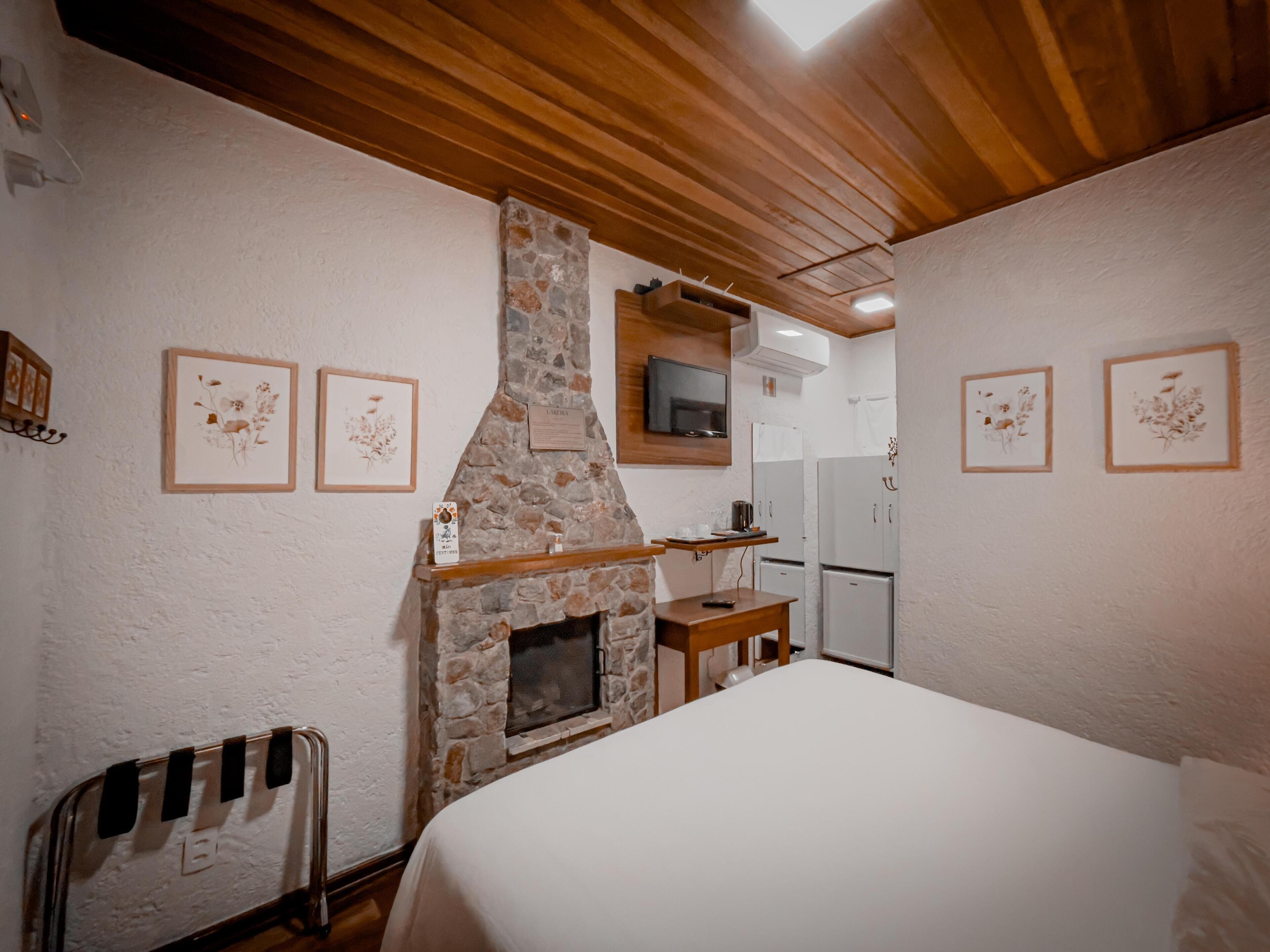 Un dormitorio con chimenea de piedra, techo de madera y paredes blancas.