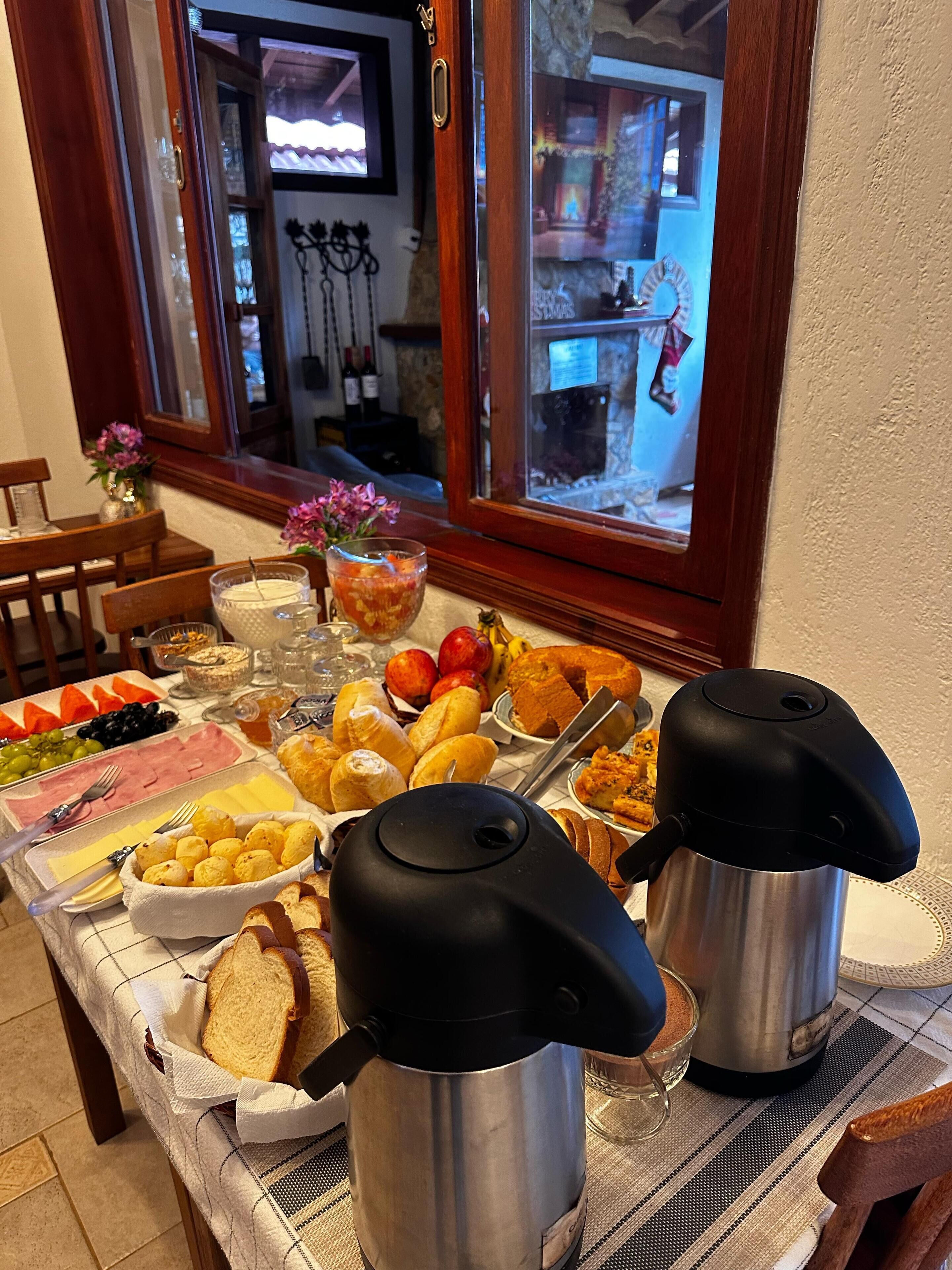 Un bufé de desayuno con diferentes opciones de comida, dos tetras eléctricos y vistas a una habitación con chimenea.