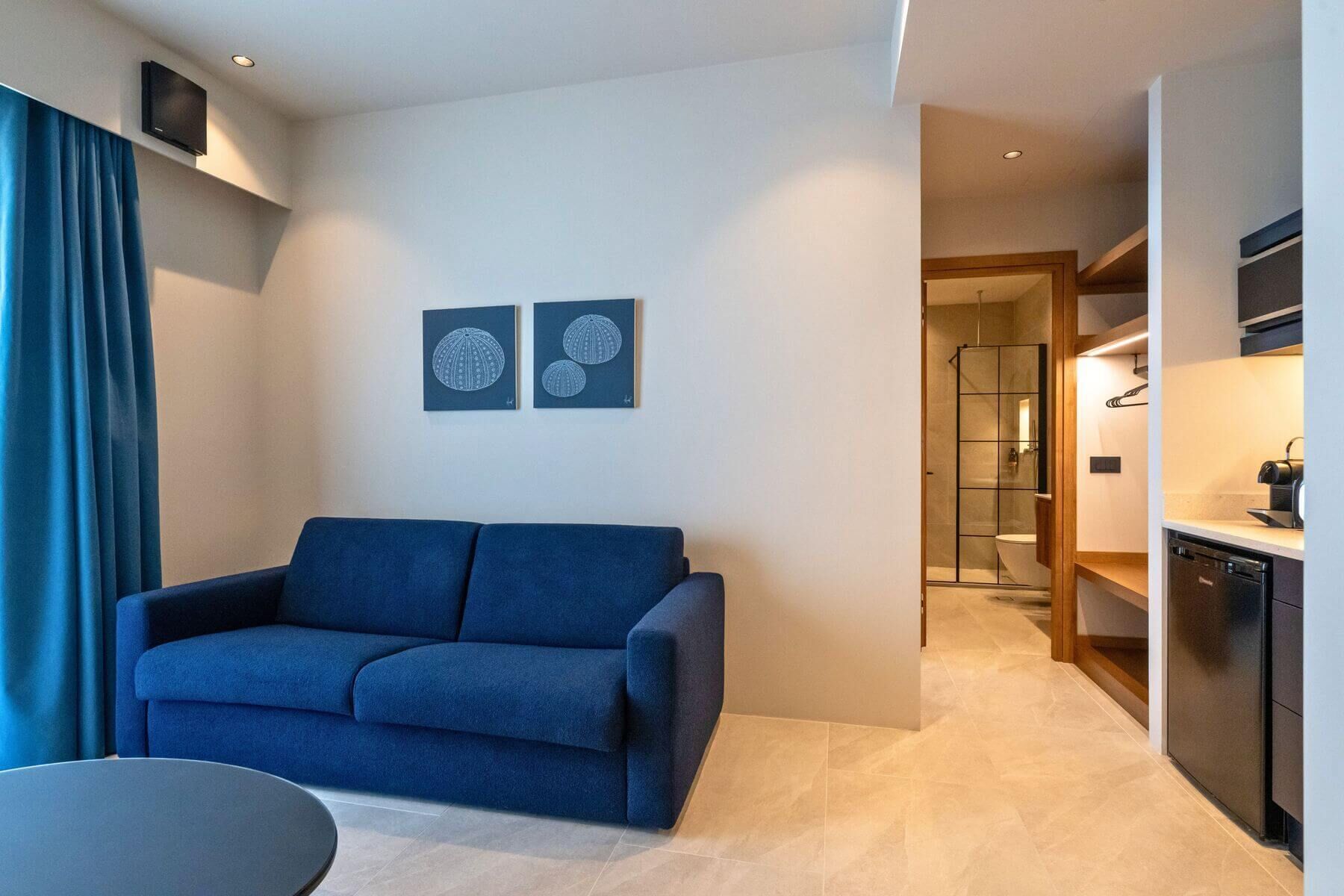 Una sala de estar moderna con un sofá azul, una pequeña mesa redonda y dos obras de arte colgadas en la pared.