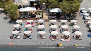 Une plage bordée de rangées de transats et de parasols, un espace café et un sentier menant à l’eau.