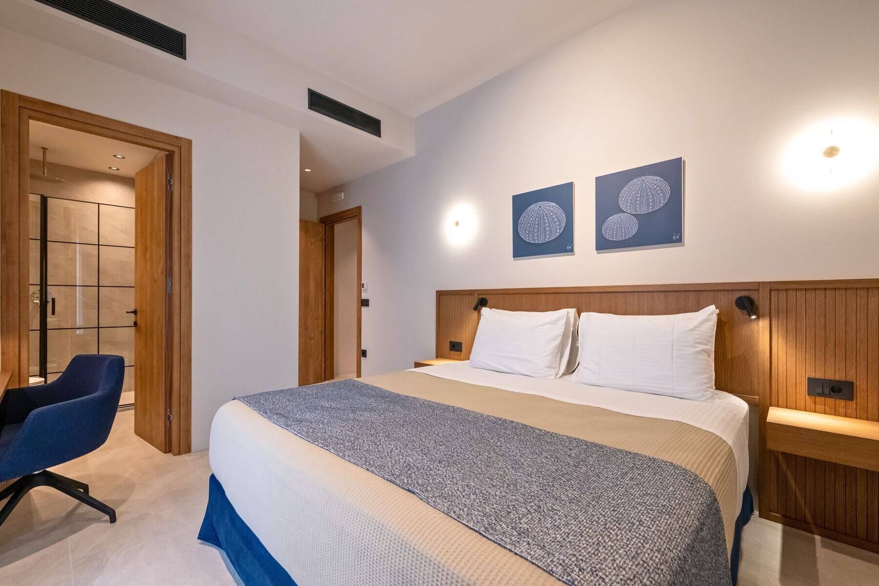 Ein Hotelzimmer mit einem großen Bett, einem Schreibtisch, einem Sessel und zwei Wandbildern.
