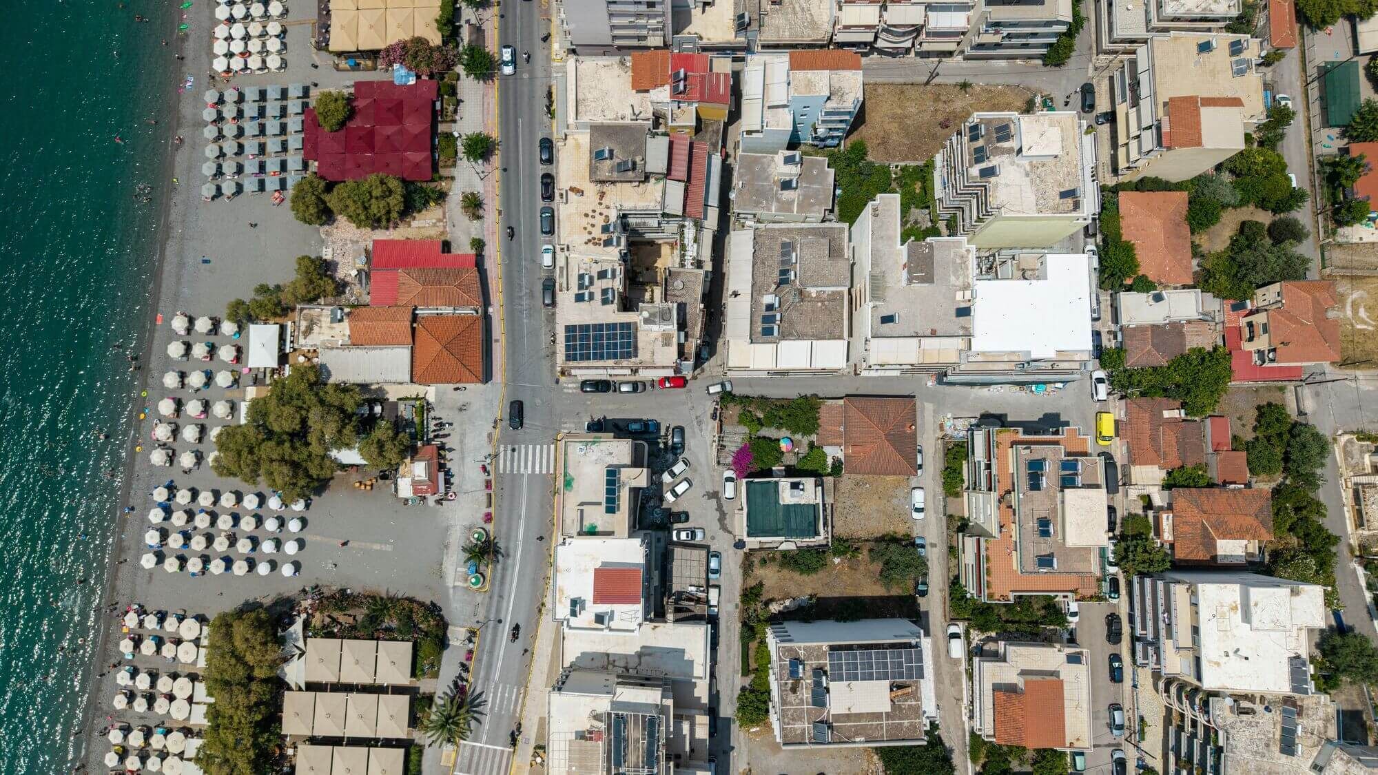 An aerial view of a coastal urban area with a beach, buildings, and parked cars.
