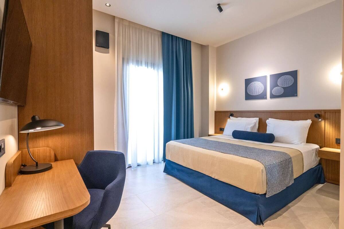 Habitación de hotel con cama, escritorio, silla, televisor y dos luces fijadas a la pared.