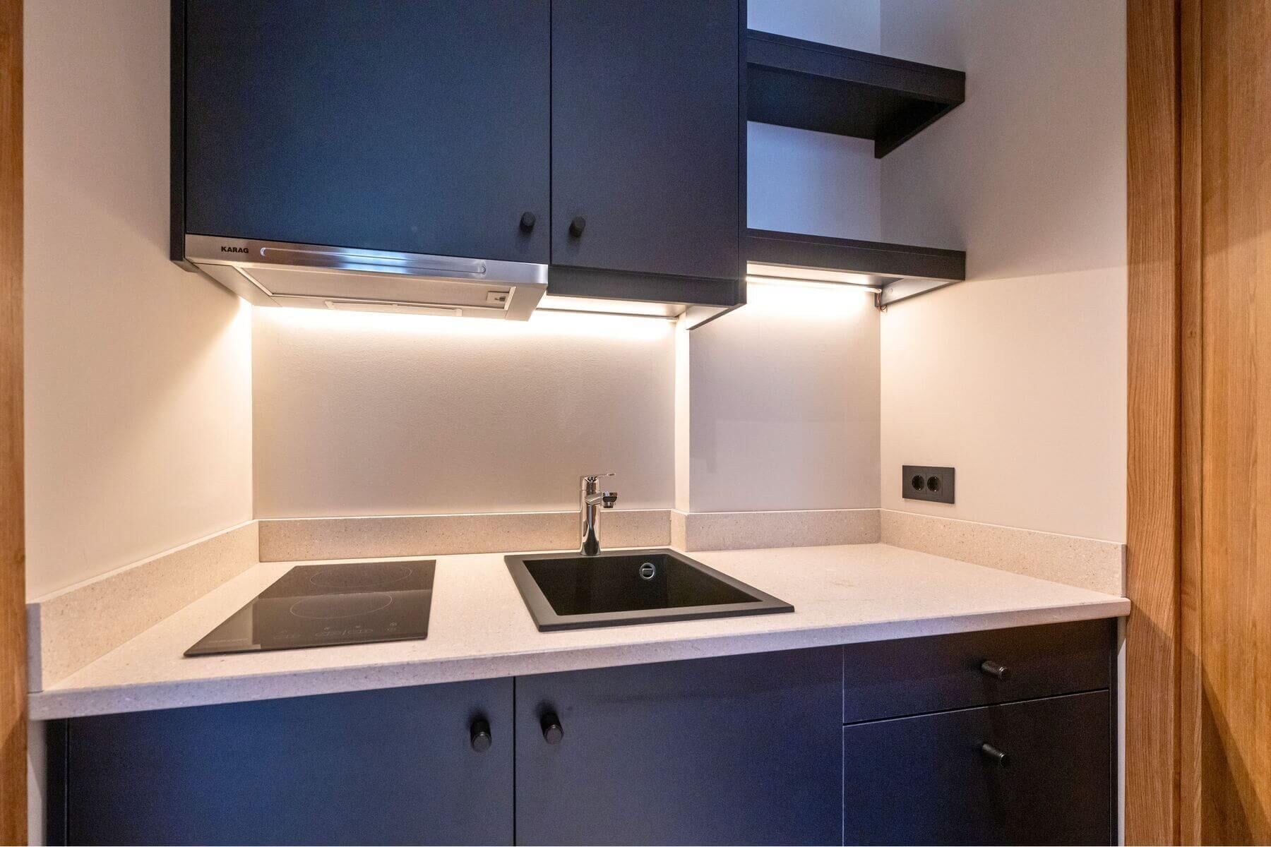 A modern kitchen with dark cabinets, a double sink, and under-cabinet lighting.
