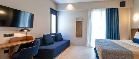 A modern hotel room with a desk, a sofa, a bed, and a TV.