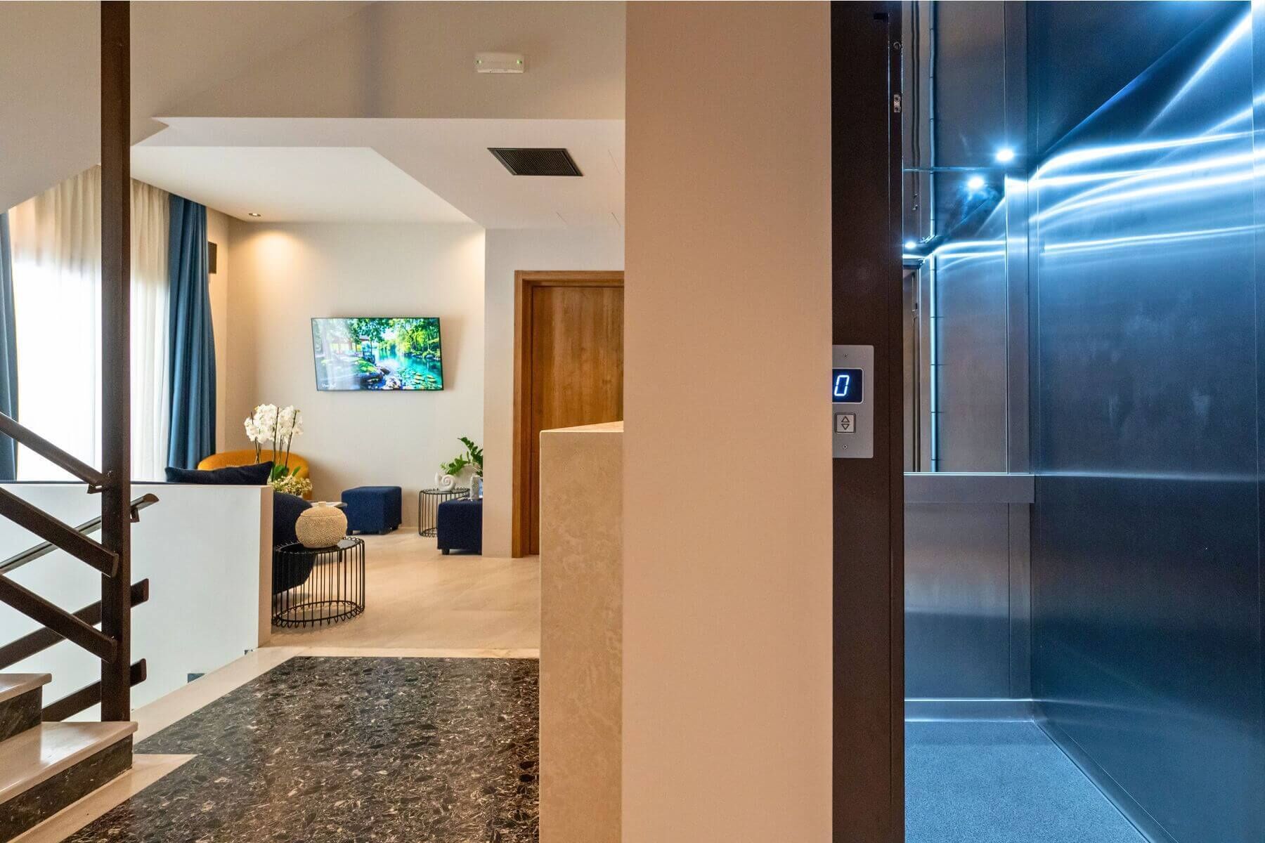 Un moderno vestíbulo de hotel con una escalera, un televisor de pantalla plana y un panel digital de ascensor.