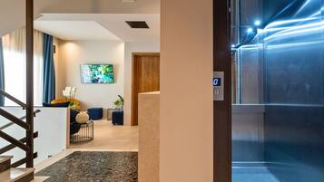 Un moderno vestíbulo de hotel con una escalera, un televisor de pantalla plana y un panel digital de ascensor.