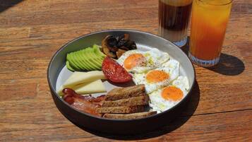 A breakfast plate with eggs, bacon, avocado, tomato, cheese, and toast on a wooden table.