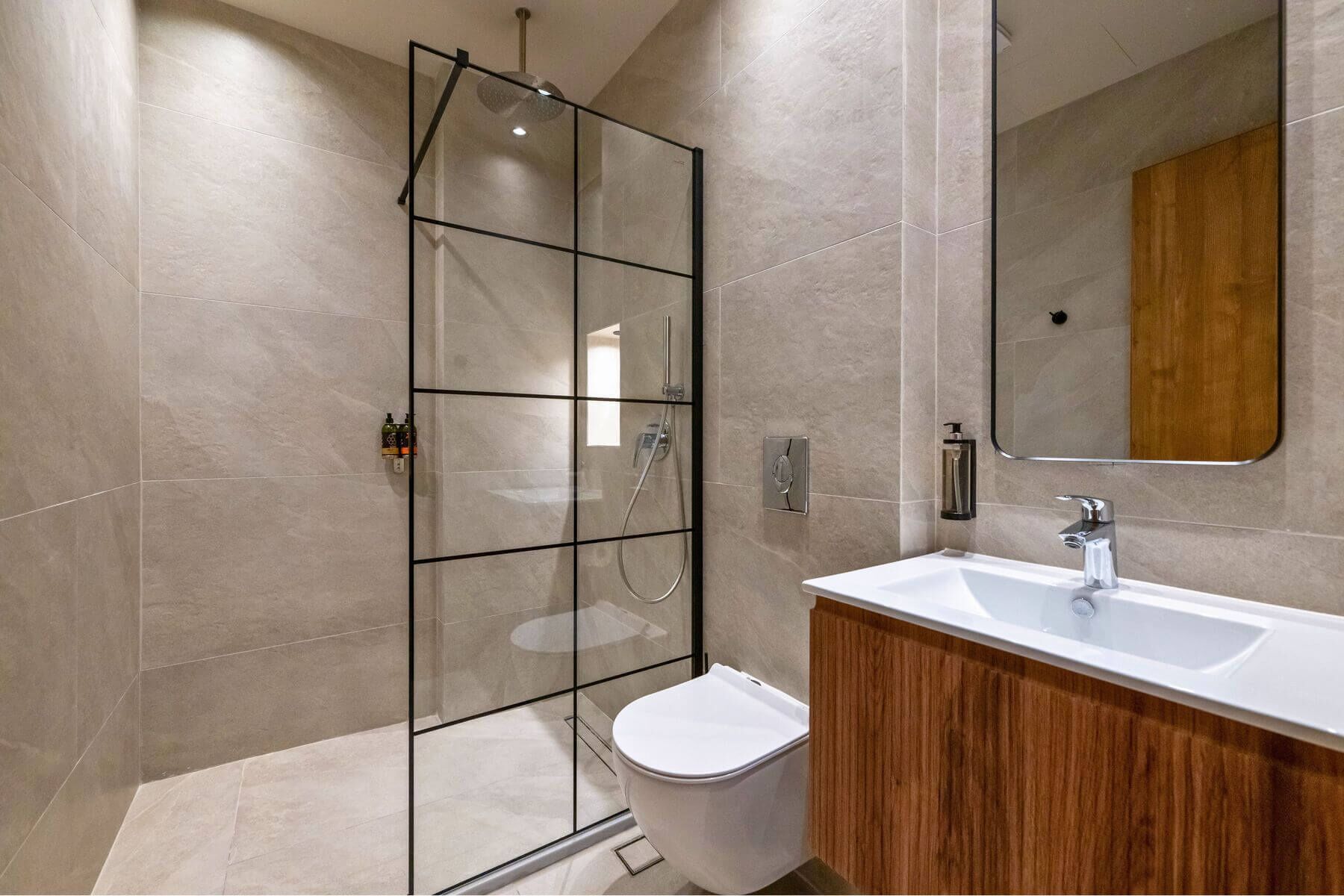A modern bathroom with a glass shower enclosure, a white toilet, and a wooden vanity with a white sink.