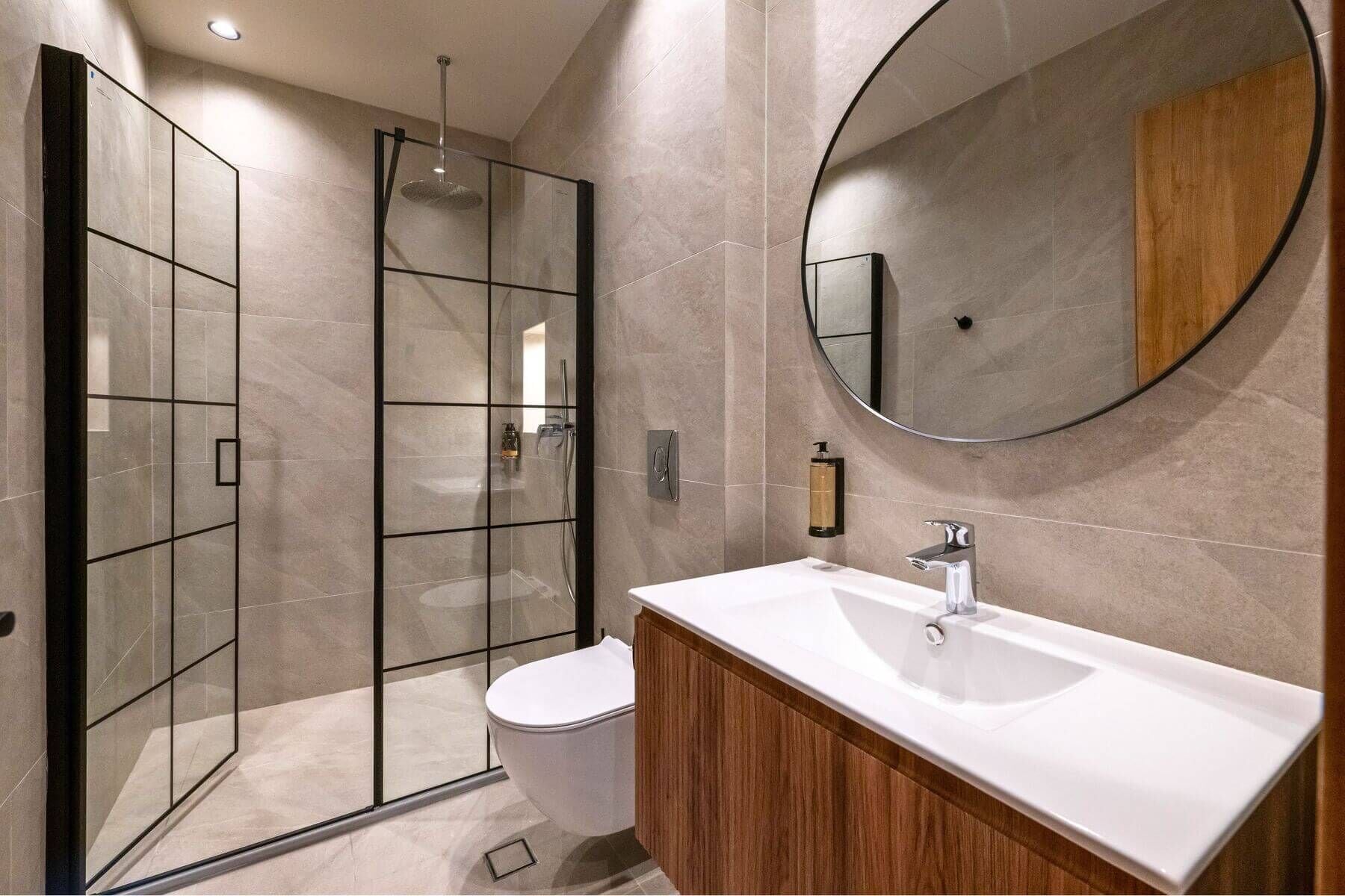 A modern bathroom with a glass shower enclosure, a white toilet, a wooden vanity, and a large mirror.