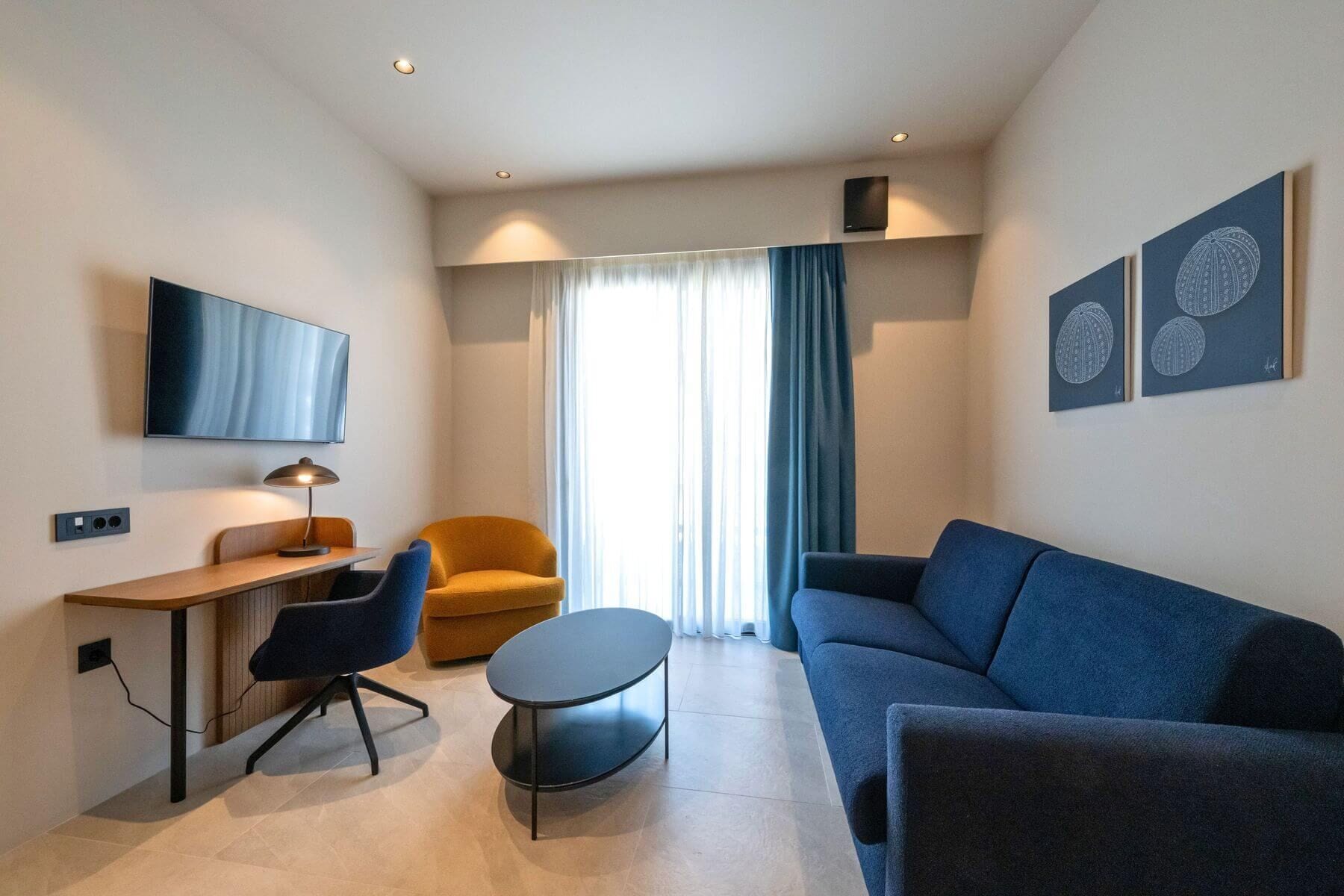 A modern living room with a sofa, a desk, a chair, a TV, and artwork on the wall.